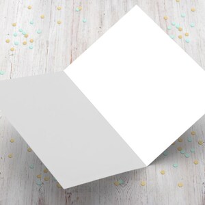 以下が含まれることがあります： 白い木製の表面に、青い金色のコンフェッティが散らばっている、折り畳まれた端のある空白の白いカードです。