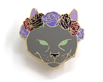 May include: A gray cat face with green eyes wearing a flower crown. The crown is made of purple, red, and black roses.