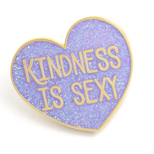 K&ouml;nnte beinhalten: Herzf&ouml;rmige Emaille-Anstecknadel mit glitzerndem, lavendelfarbenem Hintergrund und goldfarbenem Rand. Die Anstecknadel tr&auml;gt den Text "KINDNESS IS SEXY" in goldfarbenen Buchstaben. Die Anstecknadel ist ein dekoratives Accessoire.