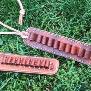 Könnte beinhalten: Zwei Leder-Munitionshalter mit einem braunen Lederriemen. Die Halter sind mit braunen Patronen gefüllt. Die Halter befinden sich auf einer grünen Grasfläche.