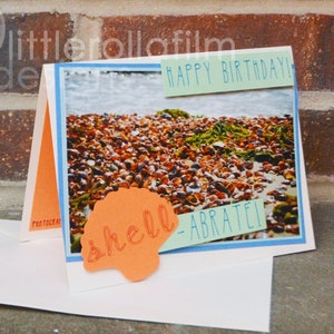 May include: A handmade birthday card with a seashell design. The card features a photo of a beach with seashells and the text "Happy Birthday!" and "Shell-ebrate!"