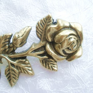 Puede incluir: Una rosa de metal dorado con hojas, elaborada en un estilo realista. La rosa es una pieza decorativa con un dise&ntilde;o detallado.