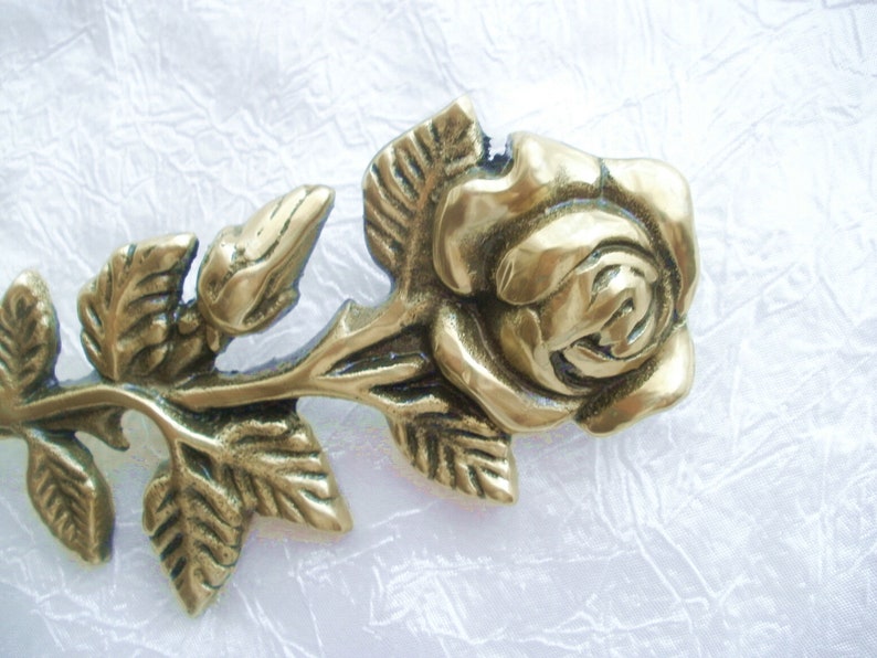 Puede incluir: Una rosa de metal dorado con hojas, elaborada en un estilo realista. La rosa es una pieza decorativa con un dise&ntilde;o detallado.