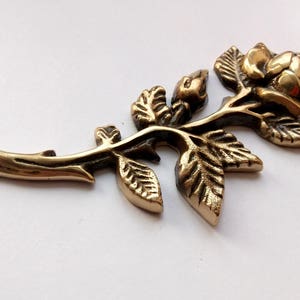 Puede incluir: Una rosa de metal de color dorado con hojas y tallo. La rosa es detallada y tiene un aspecto realista.