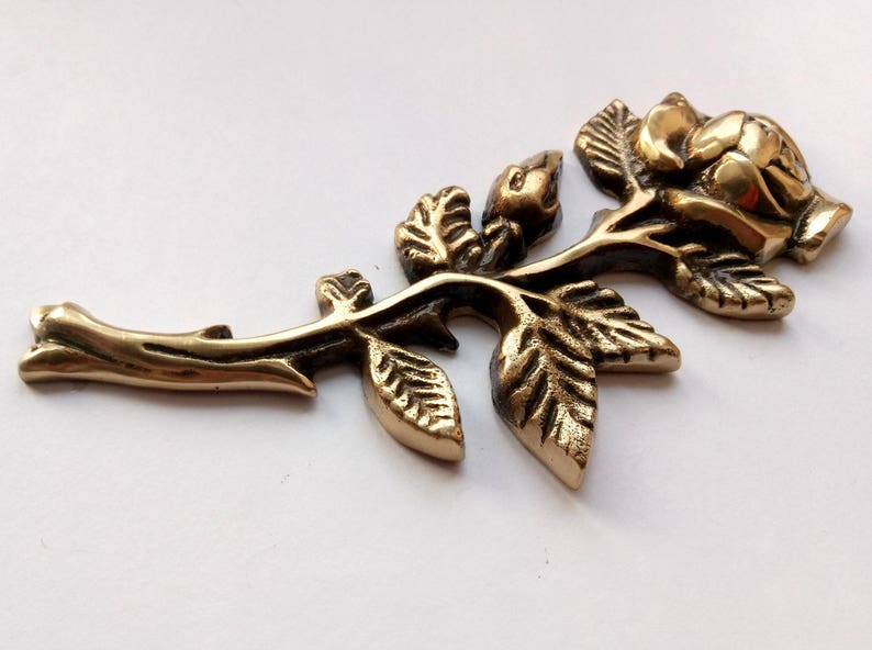Puede incluir: Una rosa de metal de color dorado con hojas y tallo. La rosa es detallada y tiene un aspecto realista.