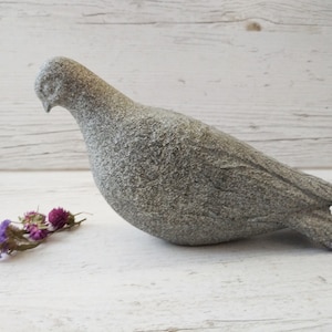 May include: A grey stone dove sculpture with a textured surface. The dove is perched on a white wooden surface.