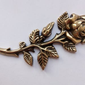Puede incluir: Una rosa de metal dorado con hojas y tallo detallados. La rosa es una pieza decorativa de estilo vintage.