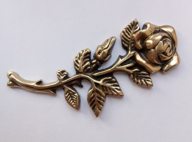 Puede incluir: Una rosa de metal dorado con hojas y tallo detallados. La rosa es una pieza decorativa de estilo vintage.