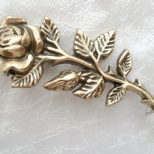 Puede incluir: Un broche de metal dorado en forma de rosa con un dise&ntilde;o detallado de una rosa con hojas y espinas.