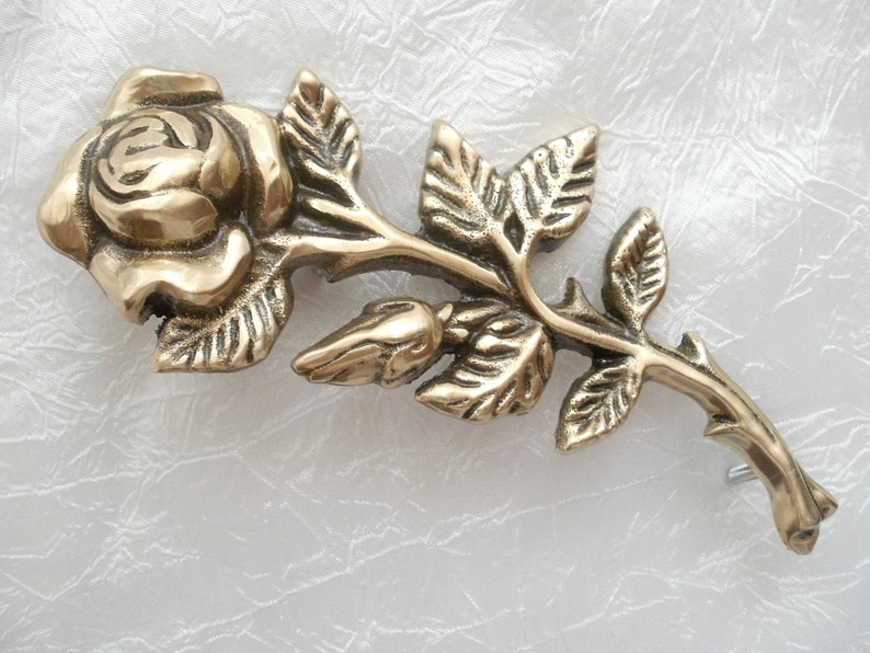 Puede incluir: Un broche de metal dorado en forma de rosa con un dise&ntilde;o detallado de una rosa con hojas y espinas.