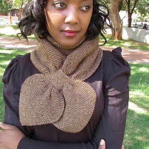 May include: A brown knitted scarf with a large bow in the front. The scarf is worn by a person with dark hair and brown eyes.