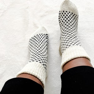 Puede incluir: Un par de calcetines blancos con un patr&oacute;n geom&eacute;trico blanco y negro. Los calcetines se llevan puestos en los pies de una persona.