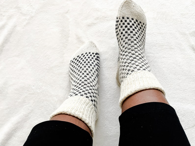 Puede incluir: Un par de calcetines blancos con un patr&oacute;n geom&eacute;trico blanco y negro. Los calcetines se llevan puestos en los pies de una persona.