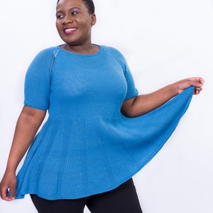 May include: A woman wearing a blue knitted top with a flared hem. The top has short sleeves and a round neckline.