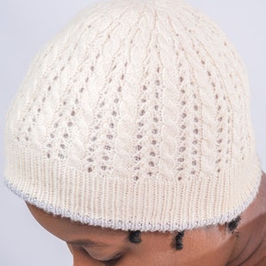 May include: A cream-colored knitted beanie with a cable knit pattern and a light gray trim.