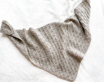 May include: A light brown knitted shawl with a delicate openwork pattern. The shawl is folded in half and laid flat on a white surface.
