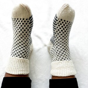 Puede incluir: Un par de calcetines blancos de punto con un patr&oacute;n geom&eacute;trico blanco y negro. Los calcetines tienen un pu&ntilde;o de canal&eacute;.
