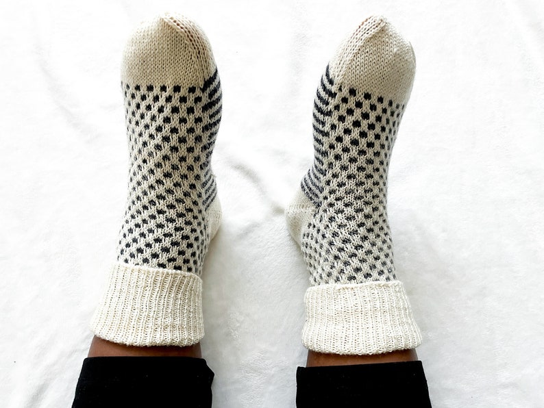 Puede incluir: Un par de calcetines blancos de punto con un patr&oacute;n geom&eacute;trico blanco y negro. Los calcetines tienen un pu&ntilde;o de canal&eacute;.