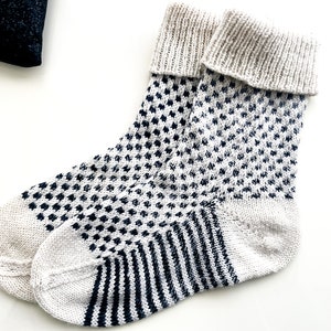 Puede incluir: Un par de calcetines de punto blanco con un patr&oacute;n geom&eacute;trico blanco y negro. Los calcetines tienen un pu&ntilde;o acanalado y un patr&oacute;n de rayas contrastantes en el pie.