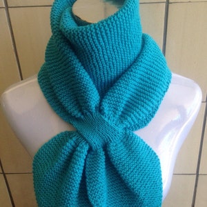 May include: A turquoise knitted scarf with a cowl neck design. The scarf is folded in a bow shape and is displayed on a white mannequin.