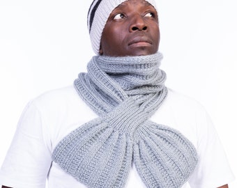 May include: A man wearing a gray and black striped knit hat and a gray knit scarf. The scarf is tied in a loose knot around his neck.