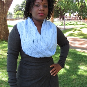 May include: A woman wearing a dark gray dress with a light blue knitted scarf. The scarf has a delicate, openwork pattern.