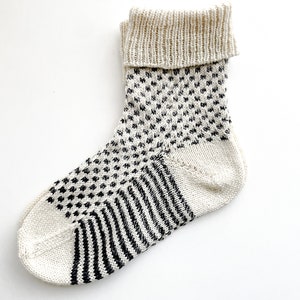 Puede incluir: Calcetines de punto blanco con un patr&oacute;n geom&eacute;trico blanco y negro. Los calcetines tienen un pu&ntilde;o doblado.