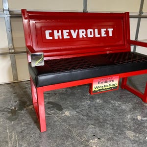 May include: A red bench with a black, diamond-stitched seat and a back featuring the white "CHEVROLET" logo. The bench has red legs and armrests. A sign that reads "INDIANA Emilie's Workshop" is attached to the front.