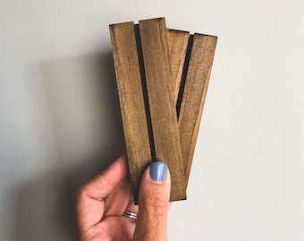 Puede incluir: Tres piezas rectangulares de madera teñida, presentadas sobre un fondo gris claro. Las piezas están dispuestas en abanico, con ranuras visibles. La veta de la madera es visible, agregando textura. Tinte marrón cálido.