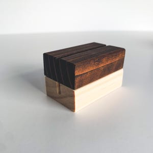 May include: A wooden sign holder with a dark brown top and a light brown base. The holder has a slot in the middle for displaying a sign.