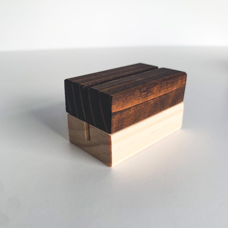 May include: A wooden sign holder with a dark brown top and a light brown base. The holder has a slot in the middle for displaying a sign.