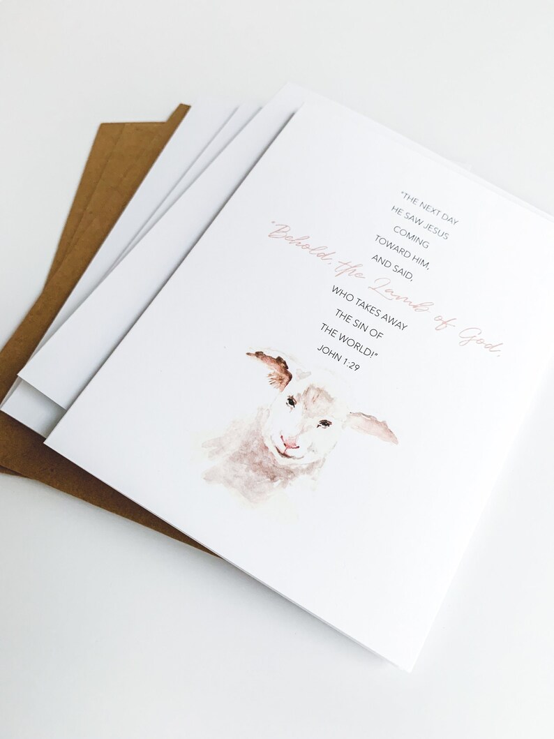 K&ouml;nnte beinhalten: Eine Aquarell-Illustration eines wei&szlig;en Lamms mit rosa Nase. Der Text "Behold, the Lamb of God." ist in rosa Schrift geschrieben. Der Text "The next day he saw Jesus coming toward him, and said, "Who takes away the sin of the world!" John 1:29" ist in schwarzer Schrift geschrieben.