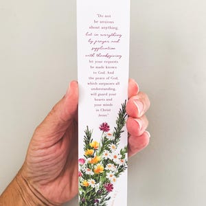 May include: A rectangular white paper bookmark featuring a floral illustration at the bottom with red, yellow, and white flowers and green foliage. The text reads: Do not be anxious about anything, but in everything by prayer and supplication.