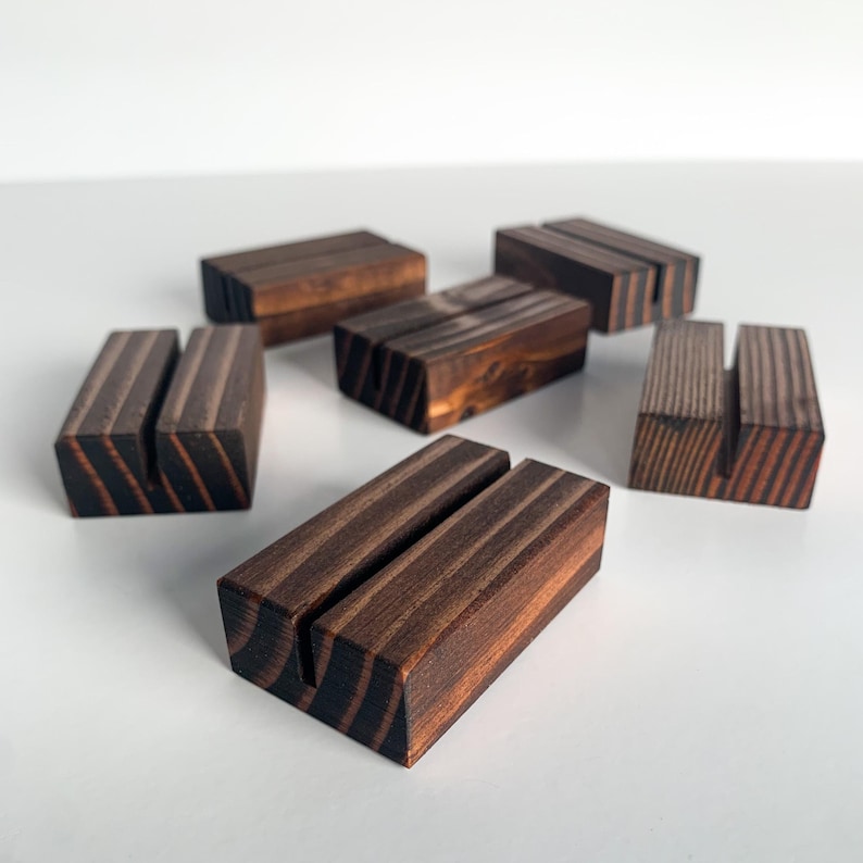 May include: Six wooden card holders with a dark brown stain. The holders have a slot in the center for holding cards or photos.