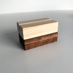 May include: A wooden sign holder with a natural wood finish on top and a dark stained wood base.
