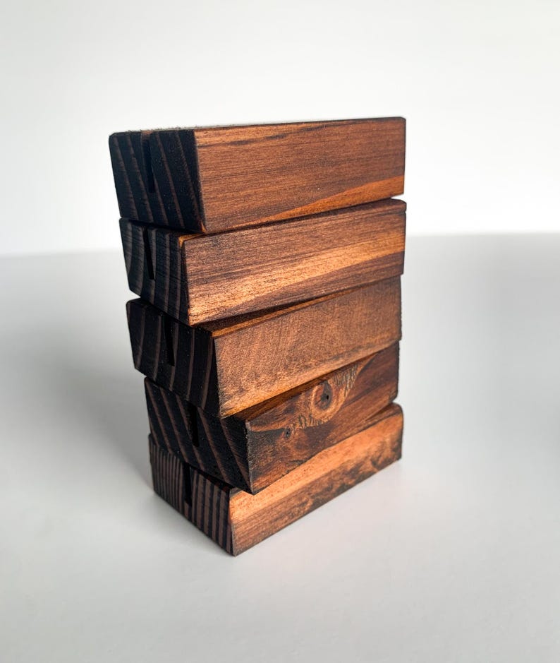 May include: A stack of six wooden blocks, each with a dark brown stain and a slightly different grain pattern. The blocks are stacked in a staggered pattern, creating a unique and rustic look.