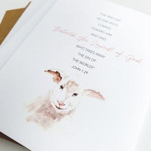 K&ouml;nnte beinhalten: Ein Aquarellbild eines wei&szlig;en Lammes mit rosa Nase. Der Text "Behold, the Lamb of God. Who takes away the sin of the world!" ist in rosa Schrift geschrieben. Der Text "John 1:29" ist in schwarz unter dem rosa Text geschrieben.