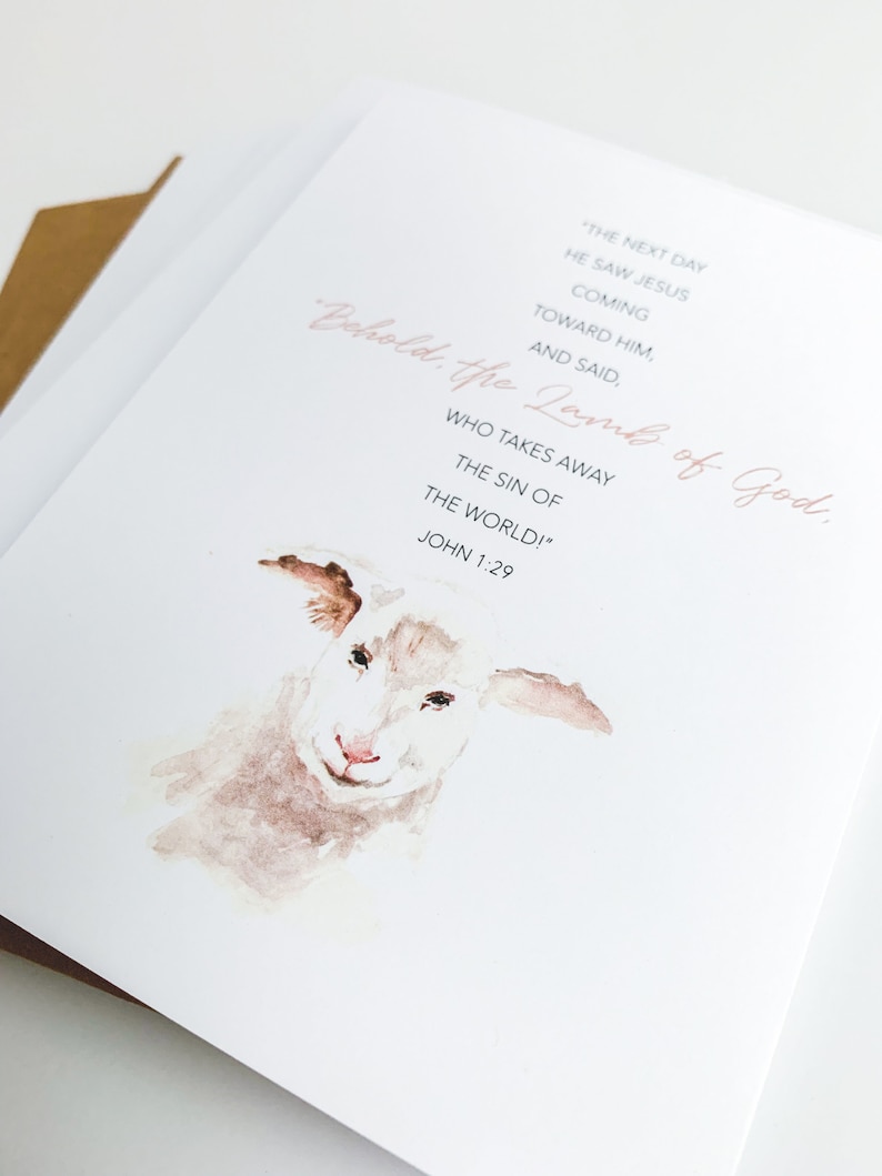 K&ouml;nnte beinhalten: Ein Aquarellbild eines wei&szlig;en Lammes mit rosa Nase. Der Text "Behold, the Lamb of God. Who takes away the sin of the world!" ist in rosa Schrift geschrieben. Der Text "John 1:29" ist in schwarz unter dem rosa Text geschrieben.