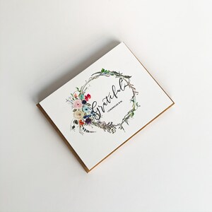 May include: A white card with a floral wreath and the word "Grateful" written in black calligraphy. The text "1 Chronicles 16:34" is written in smaller font below the word "Grateful".