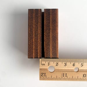 May include: A dark brown wooden sign holder with a slot for a sign. The holder is 2 inches wide and 3 inches tall.
