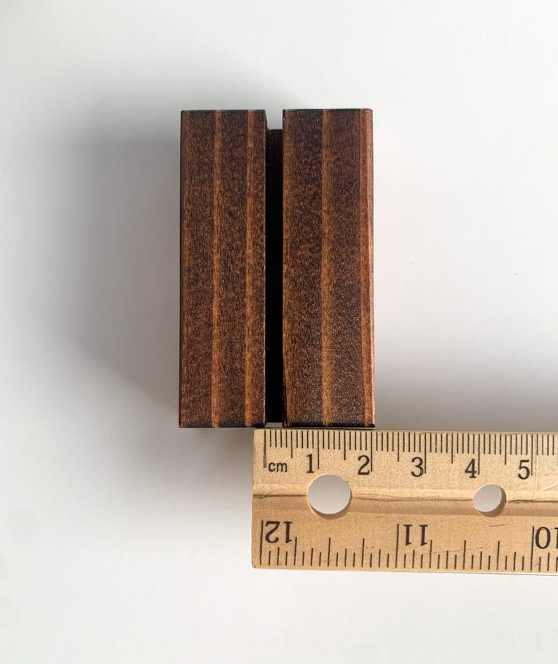 May include: A dark brown wooden sign holder with a slot for a sign. The holder is 2 inches wide and 3 inches tall.