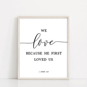 May include: A white framed print with black text that reads "We love because he first loved us. 1 John 4:19"