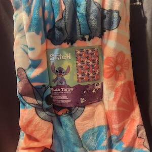 Puede incluir: Una manta de felpa con el personaje Stitch de Lilo & Stitch de Disney. La manta tiene un dise&ntilde;o floral rosa, azul y blanco con ilustraciones de Stitch. El embalaje dice "Stitch Plush Throw". La manta mide 127cm x 178cm.