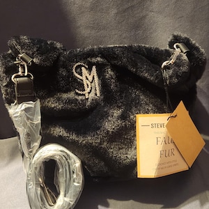 May include: Black faux fur handbag with a silver-tone chain strap and the initials "SM" in rhinestones. Includes a detachable strap and a tag that reads "FAUX FUR".