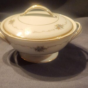 Puede incluir: Fuente de servir crema con tapa, ribete dorado y detalles florales. El plato tiene una base redondeada y un asa en la tapa. El diseño incluye un delicado estampado floral y un borde dorado.
