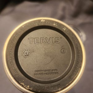May include: The circular base of a Tervis stainless steel tumbler with a 30oz capacity. The black bottom features the text 'TERVIS', 'Designed in Florida', 'DISHWASHER SAFE', 'DO NOT MICROWAVE', 'Made in China', and a small circular date dial.