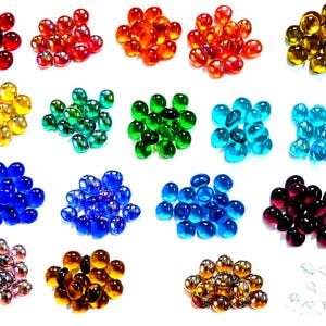 May include: A collection of small, smooth, rounded glass gems arranged in twenty distinct color groups. The assortment includes red, orange, yellow, green, teal, blue, purple, brown, gold, and clear translucent stones with a polished finish.