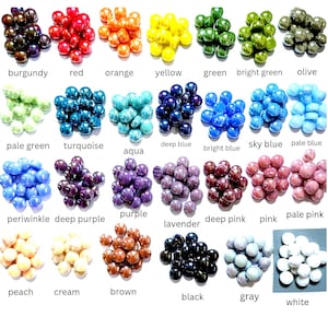 May include: A collection of small, round, smooth glass beads arranged in twenty-eight distinct color groups. Each group is labeled with its corresponding color name, including burgundy, red, orange, yellow, green, bright green, olive, pale green, turquoise, aqua, deep blue, bright blue, sky blue, pale blue, periwinkle, deep purple, purple, lavender, deep pink, pink, pale pink, peach, cream, brown, black, gray, and white.