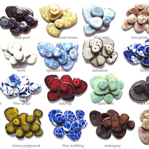 Puede incluir: Una colección de piedras decorativas de cerámica en varios colores y patrones. La imagen muestra diseños como vides azules, piscina profunda, piedras del desierto y pétalos de rosa. Cada piedra tiene una textura y paleta de colores únicas.
