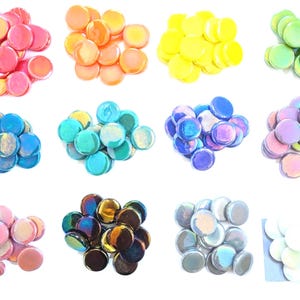 May include: A collection of twelve distinct piles of small, round, flat glass cabochons arranged in a grid. Each pile features a different color, including pink, orange, yellow, green, blue, teal, purple, lavender, light pink, dark metallic, gray, and white.